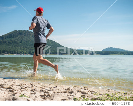 Running man in water of lake or sea along sandy beach Running man in water of lake or sea along sandy beach 69641178