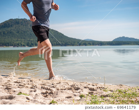 Man is running in lakeand splashing water around him Man is running in lakeand splashing water around him 69641179