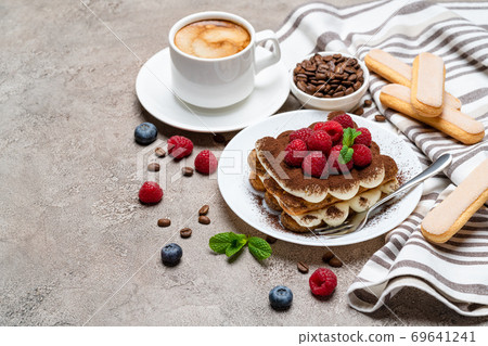 portion of Classic tiramisu dessert with raspberries and cup of coffee on grey concrete background 69641241