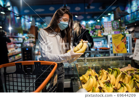 The girl with surgical mask is going to buy bananas. The girl with surgical mask is going to buy bananas. 69644209