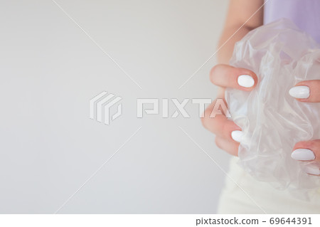 Beautiful young female hands with manicure hold a plastic oilcloth for packaging and construction. Green packaging and waste recycling concept Beautiful young female hands with manicure hold a plastic oilcloth for packaging and construction. Green packaging and waste recycling concept 69644391