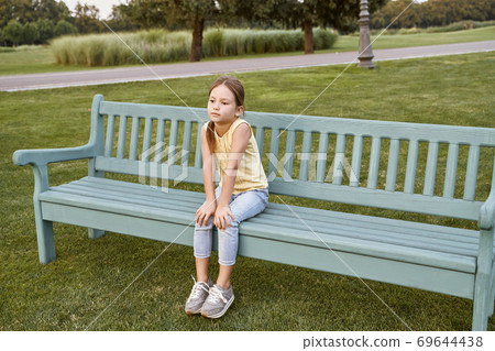 Cute little girl sitting on a wooden bench in park, child spending time outdoors Cute little girl sitting on a wooden bench in park, child spending time outdoors 69644438