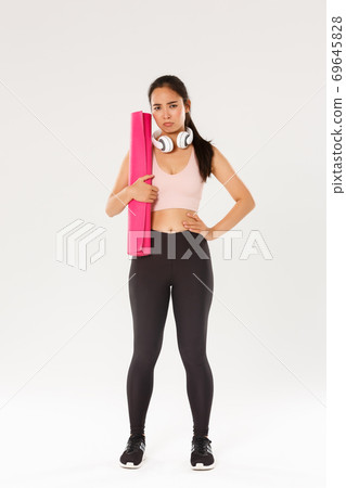 Full length of gloomy and upset cute brunette asian fitness girl in sportswear, sulking while holding rubber mat for yoga classes, looking disappointed as gym closed during covid-19 quarantine 69645828