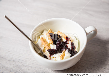 Vanilla ice cream with blackberry jam in a white cup on a wooden light background 69653198