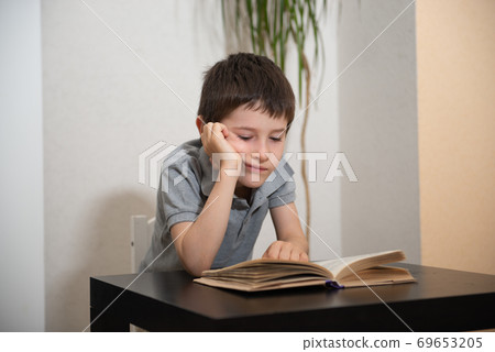 A schoolboy a bored face reads a book A schoolboy a bored face reads a book 69653205