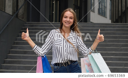 Trendy girl holding shopping bags and showing thumbs up. Rejoicing with good holiday sale discounts 69653369