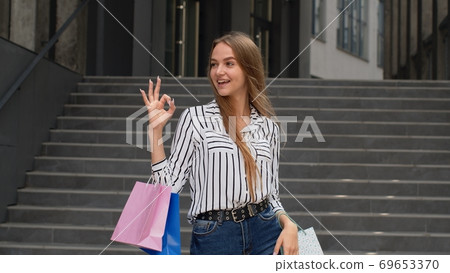 Stylish girl holding shopping bags and showing OK sign. Rejoicing with good holiday sale discounts 69653370
