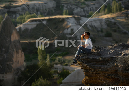 man sitting on cliff and looks into the distance. man sitting on cliff and looks into the distance. 69654030