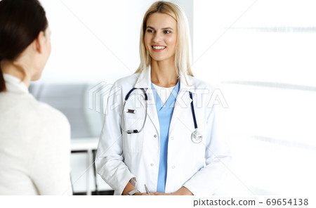 Woman-doctor at work in hospital is happy to communicate with female patient. Blonde physician checks medical history record and exam results. Medicine concept Woman-doctor at work in hospital is happy to communicate with female patient. Blonde physician checks medical history record and exam results. Medicine concept 69654138