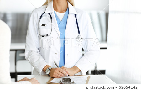 Unknown woman-doctor and patient in hospital. Blonde physician controls medication history records and exam results while using clipboard, close-up. Medicine concept Unknown woman-doctor and patient in hospital. Blonde physician controls medication history records and exam results while using clipboard, close-up. Medicine concept 69654142