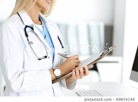 Unknown woman-doctor at work in clinic. Female physician controls medication history record and medical exam results, close-up. Medicine concept Unknown woman-doctor at work in clinic. Female physician controls medication history record and medical exam results, close-up. Medicine concept 69654148