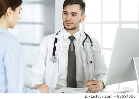 Doctor and patient. Physician man filling up medication history records form while sitting at the glass desk in medical office or clinic. Medicine and healthcare concept 69654596