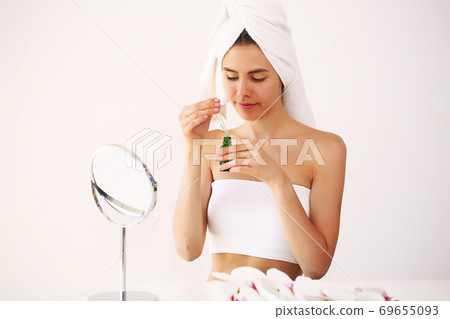 Young brunette girl takes care of her skin, standing in front of a mirror, enjoying beauty treatments for herself, smiling tenderly Young brunette girl takes care of her skin, standing in front of a mirror, enjoying beauty treatments for herself, smiling tenderly 69655093