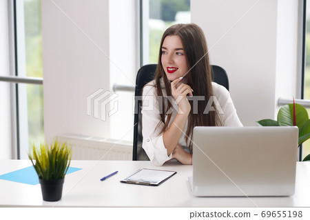 Young woman sitting at a table with a laptop in a white office. student or businesswoman 69655198