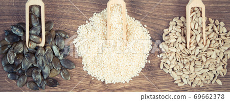 Sunflower, pumpkin and sesame seeds with wooden scoop on board, healthy nutrition concept Sunflower, pumpkin and sesame seeds with wooden scoop on board, healthy nutrition concept 69662378