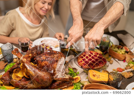 Hands of mature man cutting piece of roasted turkey on festive table by dinner 69662800