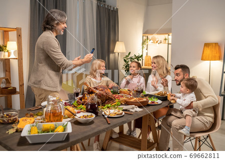 Cheerful mature man with smartphone taking photo of his big family by dinner 69662811