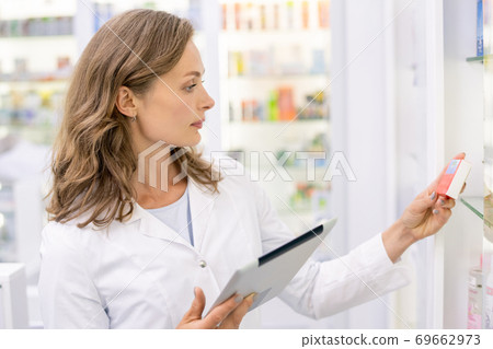 Young female pharmacist with tablet learning information about new medicaments Young female pharmacist with tablet learning information about new medicaments 69662973