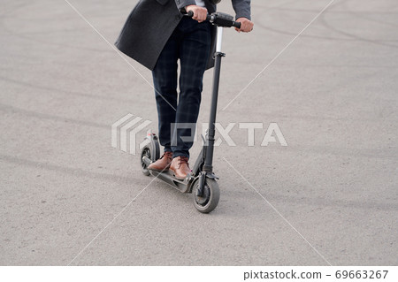 Low section of modern businessman in coat and pants riding electric scooter 69663267