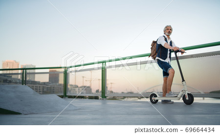 Mature man commuter with electric scooter outdoors in city, going to work. Mature man commuter with electric scooter outdoors in city, going to work. 69664434