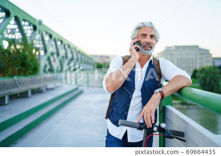 Portrait of mature man with electric scooter outdoors in city, using smartphone. Portrait of mature man with electric scooter outdoors in city, using smartphone. 69664435