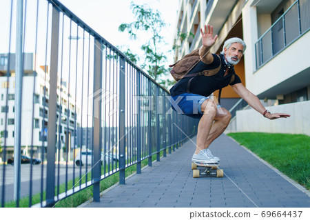 Portrait of mature man riding skateboard outdoors in city, going back to work. Portrait of mature man riding skateboard outdoors in city, going back to work. 69664437