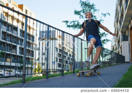 Portrait of mature man riding skateboard outdoors in city, going back to work. Portrait of mature man riding skateboard outdoors in city, going back to work. 69664438
