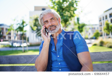 Portrait of mature man sitting outdoors in city, using smartphone. Portrait of mature man sitting outdoors in city, using smartphone. 69664457