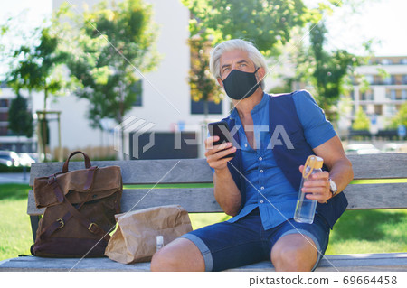 Portrait of mature man with face mask sitting outdoors in city, coronavirus concept. Portrait of mature man with face mask sitting outdoors in city, coronavirus concept. 69664458
