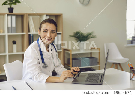 Woman doctor looking at camera during online meeting on laptop Woman doctor looking at camera during online meeting on laptop 69664674