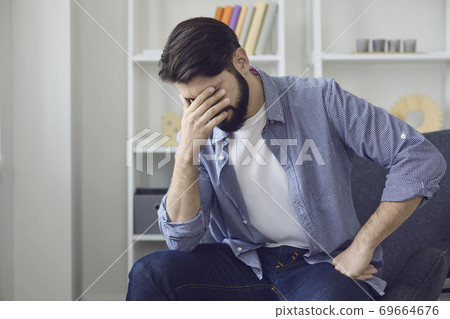 Sad man sitting at home, feeling bad and touching face with hand Sad man sitting at home, feeling bad and touching face with hand 69664676