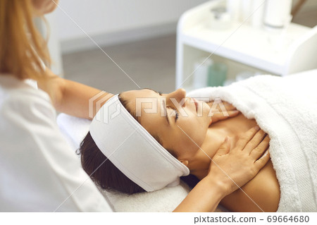 Woman patient getting manual relaxing rejuvenating massage for face and shoulders from therapist Woman patient getting manual relaxing rejuvenating massage for face and shoulders from therapist 69664680