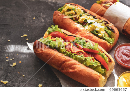 Hot dogs with various fillings. Dark background. food background with copy space. Hot dogs with mustard and ketchup, lettuce, cheese and tomatoes. Close up Hot dogs with various fillings. Dark background. food background with copy space. Hot dogs with mustard and ketchup, lettuce, cheese and tomatoes. Close up 69665667