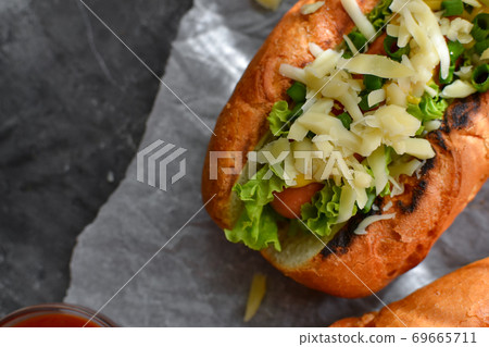 One hot dog with mustard and ketchup, lettuce, cheese and sausage. Dark background. food background with copy space. Close-up. Top view One hot dog with mustard and ketchup, lettuce, cheese and sausage. Dark background. food background with copy space. Close-up. Top view 69665711