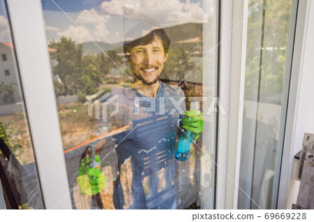 A young man cleaning the window with a window cleaner 69669228