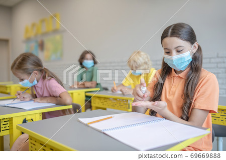 Girl in a mask spraying sanitizer on her hands 69669888