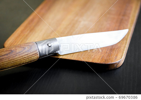 Wooden cutting board and pocket knife on a black table 69670386