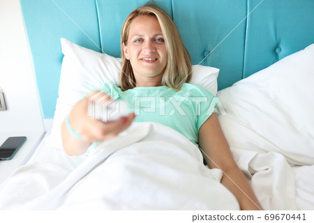 Woman lies in white bed and look TV. Woman lies in white bed and look TV. 69670441