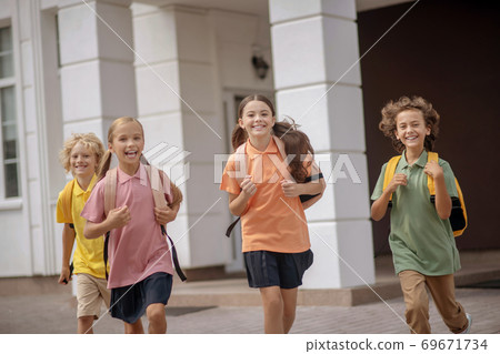 Schoolchildren with backpacks running home after lessons Schoolchildren with backpacks running home after lessons 69671734