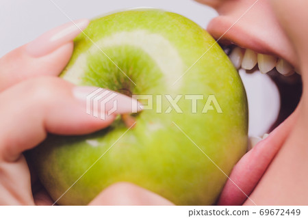 Pretty young woman with beautiful white teeth holding an apple in her hand. 69672449