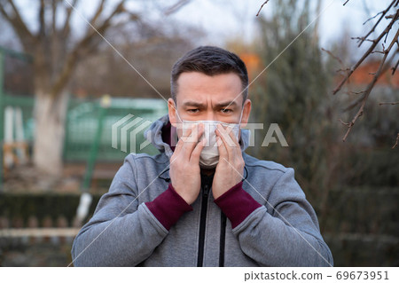 man in gray jacket put on medical mask on street. man in gray jacket put on medical mask on street. 69673951