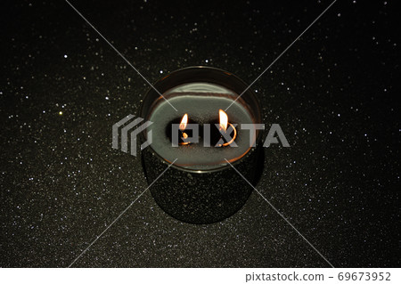 Black lighted candle with two wicks on a black background with sparkles Black lighted candle with two wicks on a black background with sparkles 69673952