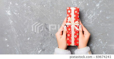 Woman hands give wrapped christmas or other holiday handmade present in colored paper . Present box, decoration of gift on gray cement table, top view with copy space Woman hands give wrapped christmas or other holiday handmade present in colored paper . Present box, decoration of gift on gray cement table, top view with copy space 69674241