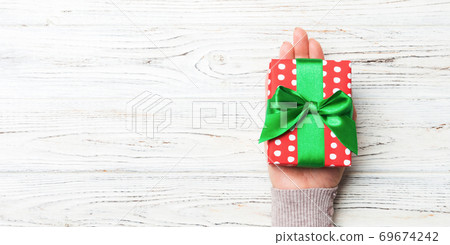 Female's hands holding striped gift box with colored ribbon on white rustic wooden background. Christmas concept or other holiday handmade present box, concept top view with copy space Female's hands holding striped gift box with colored ribbon on white rustic wooden background. Christmas concept or other holiday handmade present box, concept top view with copy space 69674242