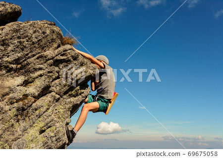 The boy is engaged in mountaineering, a child climbing a rocky mountain, a brave boy. The boy is engaged in mountaineering, a child climbing a rocky mountain, a brave boy. 69675058
