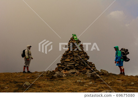 Tourists in raincoats stand on top of the mountain, Mount Brebeneskul and fog, rain clouds on the Montenegrin ridge, happy tourists. 69675080