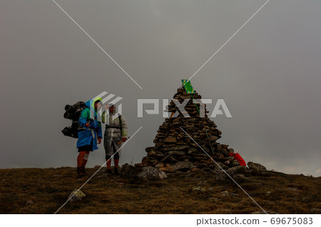 Tourists in raincoats stand on top of the mountain, Mount Brebeneskul and fog, rain clouds on the Montenegrin ridge, happy tourists. 69675083