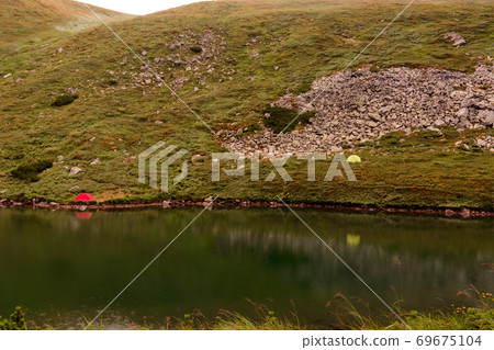 Tourists and tents near the lake, fog in the mountains near the lake, rain clouds in the Carpathians, a tent camp near the lake, Lake Brebeneskul. 69675104