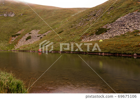 Tourists and tents near the lake, fog in the mountains near the lake, rain clouds in the Carpathians, a tent camp near the lake, Lake Brebeneskul. 69675106