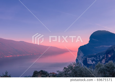 Stunning view of Lake Garda in the evening fog and the light of the setting sun. Stunning view of Lake Garda in the evening fog and the light of the setting sun. 69675571